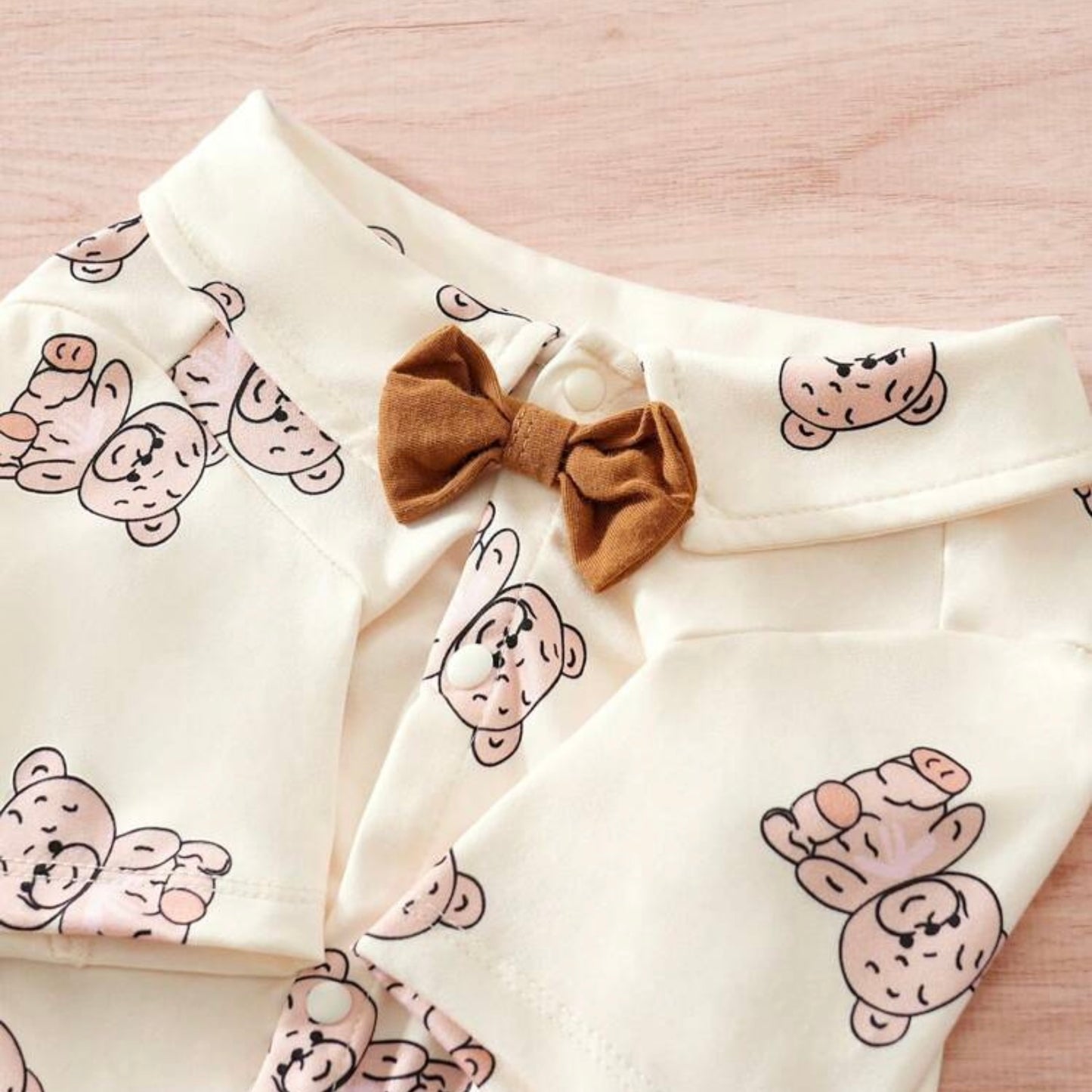 Detail of a cream-colored dog shirt with collar with a brown bow tie, featuring a teddy bear print pattern.