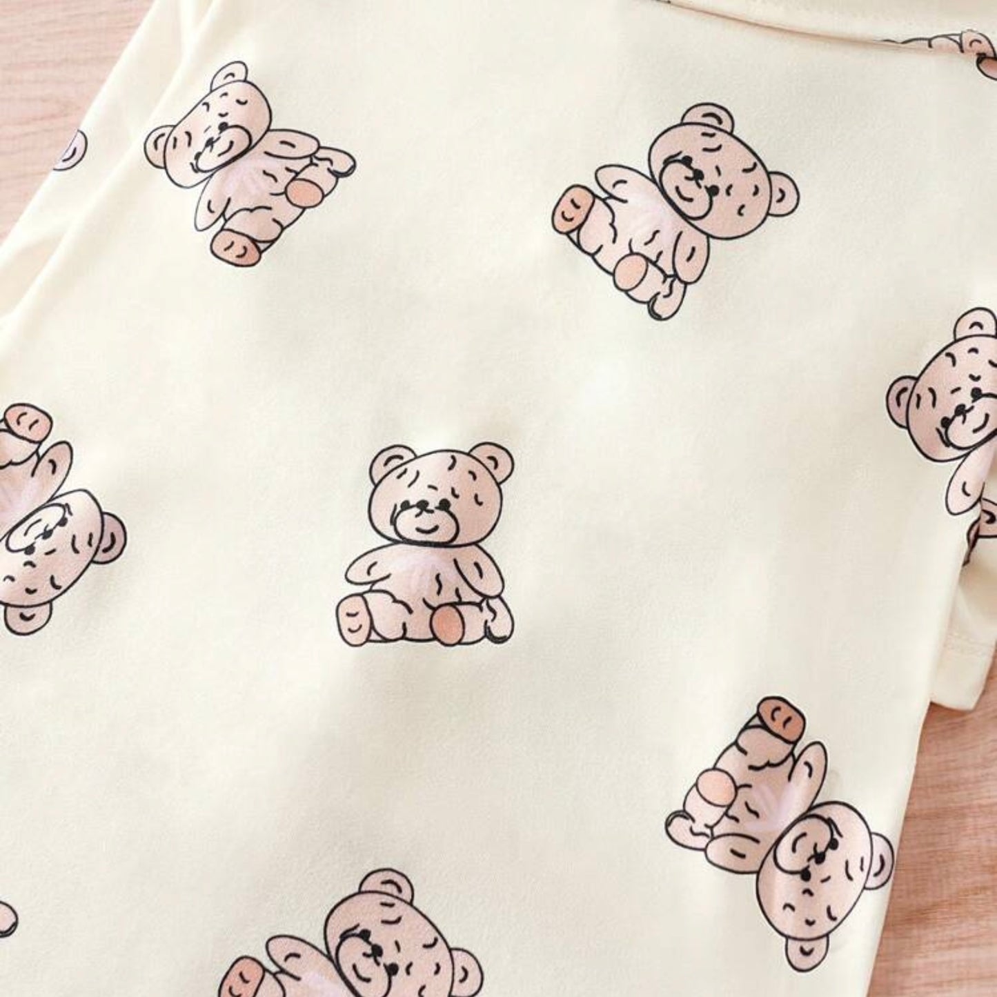 Close-up of cream-colored dog shirt with a repeating pattern of cute, smiling teddy bears sitting in various positions.
