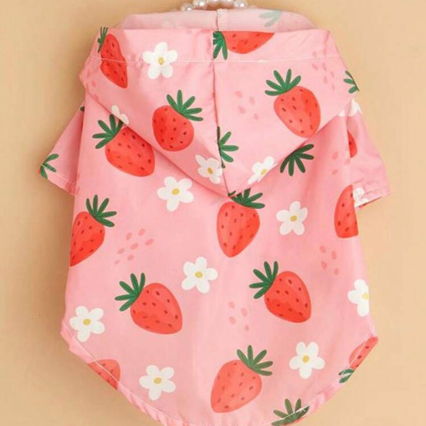 Back view of a pink dog raincoat with red strawberries and white flowers, displayed on a hanger.