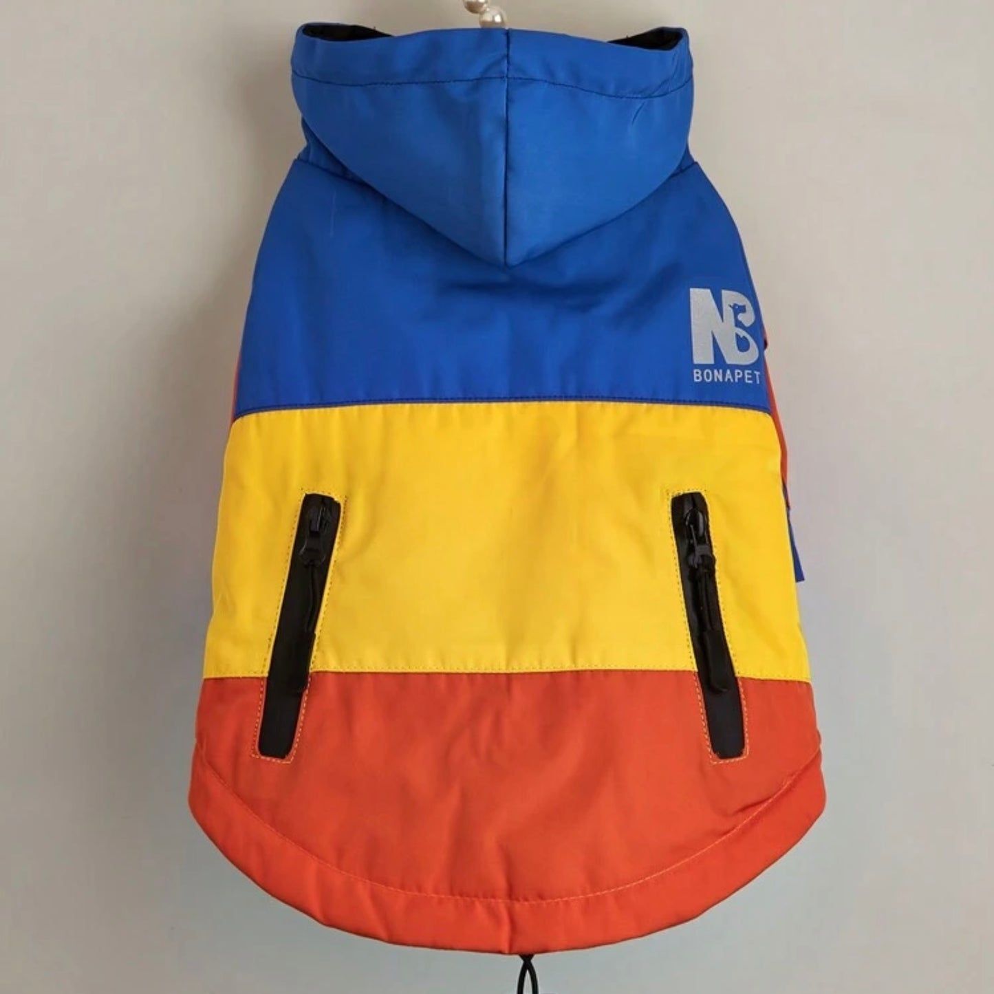 Colourblock dog jacket in blue, yellow, and red displayed on a hanger, back view.