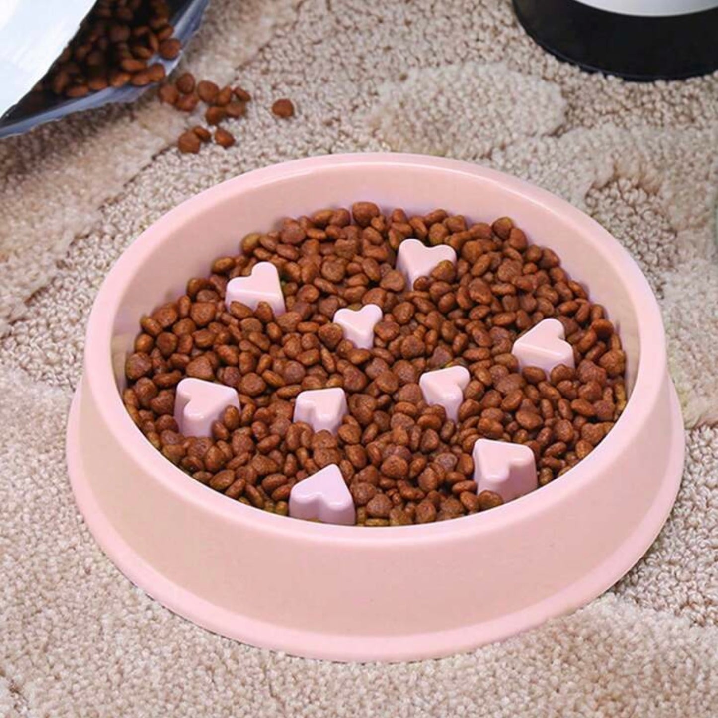 Pink slow feeder dog bowl with heart-shaped obstacles filled with dry dog kibble, placed on a textured beige carpet.
