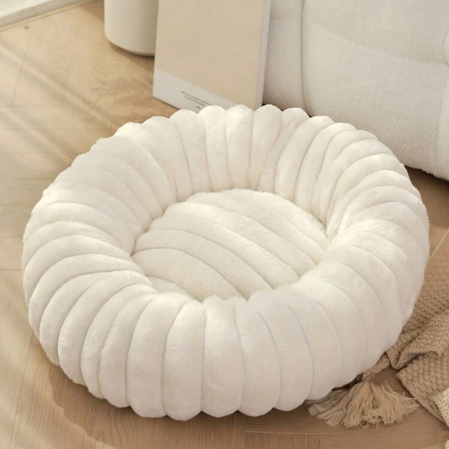 Plush ribbed donut dog bed in ivory white on a wooden floor.