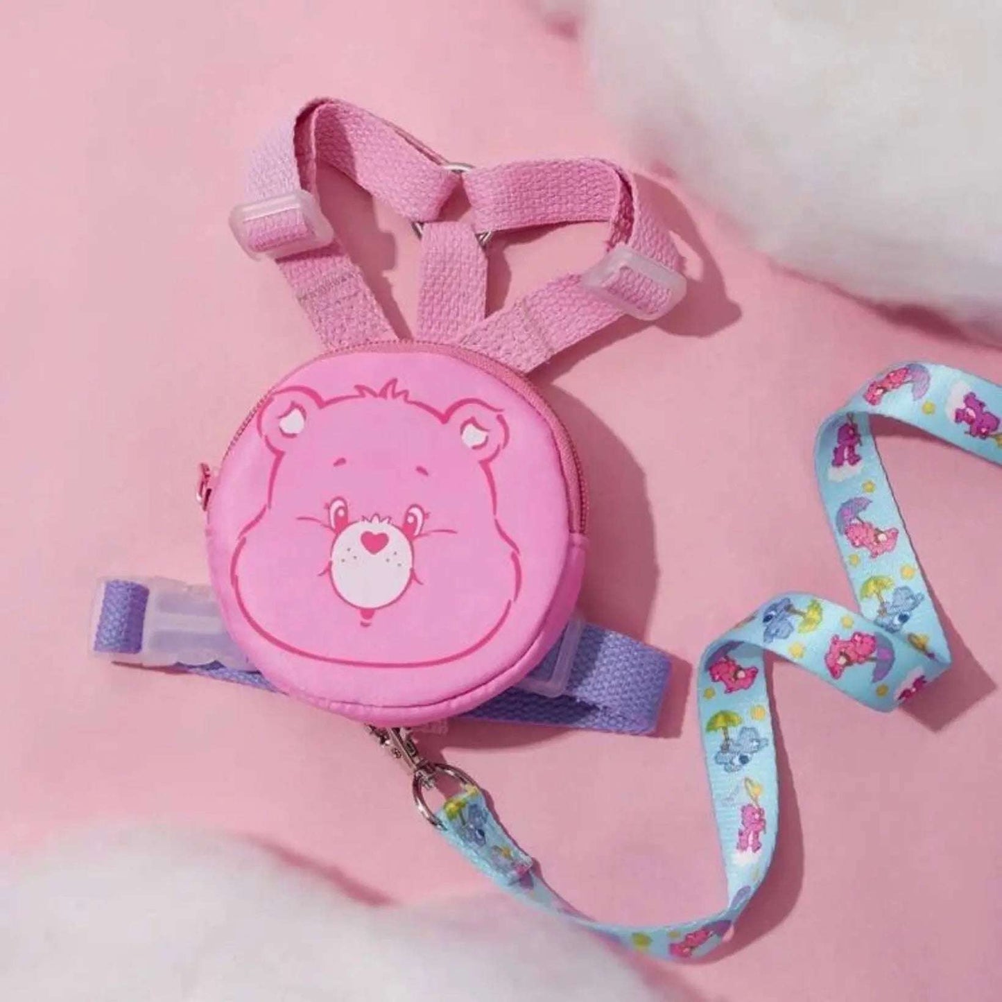 Pink Care Bears pouch attached to a purple and pink dog harness with a blue Care Bears patterned leash, arranged on a pink surface.