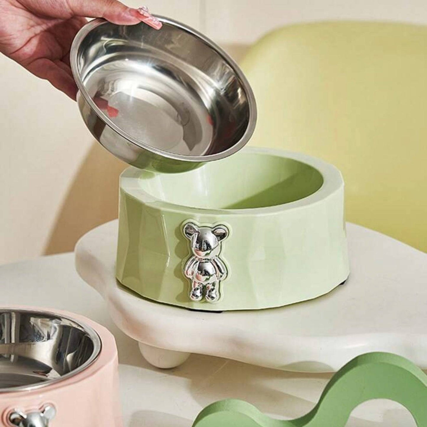 Light green geometric dog bowl with a metallic teddy bear decoration, shown with a removable stainless steel inner bowl.