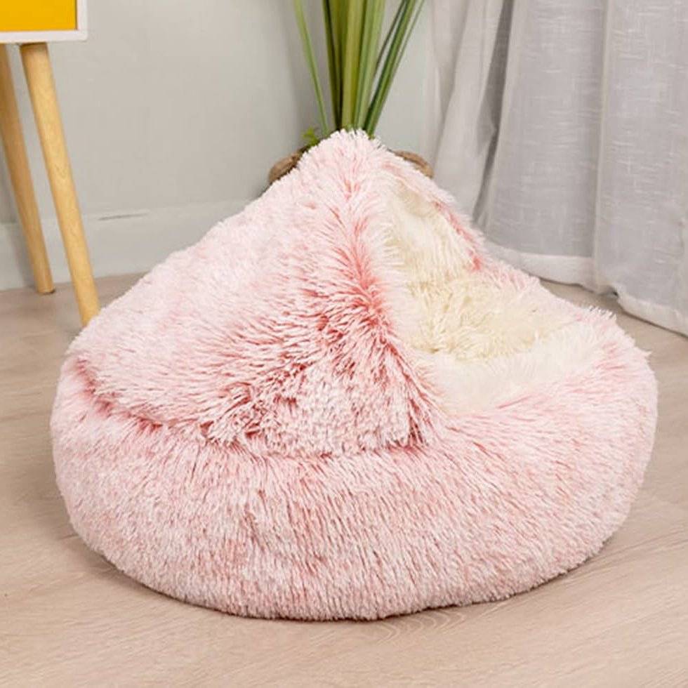 Light pink and cream plush dog cave bed with a pointed dome, placed on a light wooden floor.