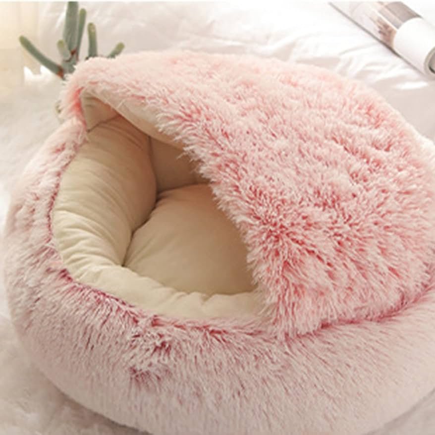 Light pink and cream plush dog cave bed with an open entrance, placed on a beige surface.