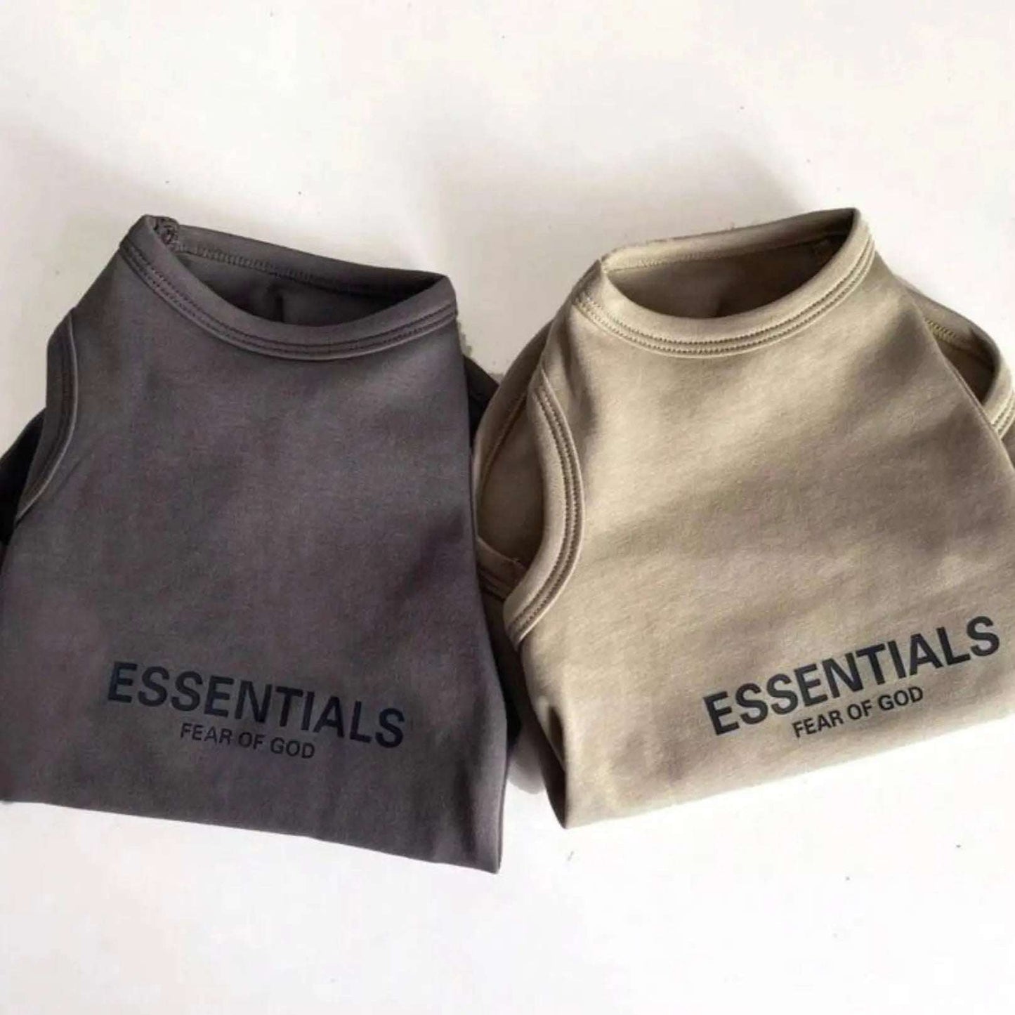 Two Fear of God Essentials dog tank tops in black and beige, laid side by side.