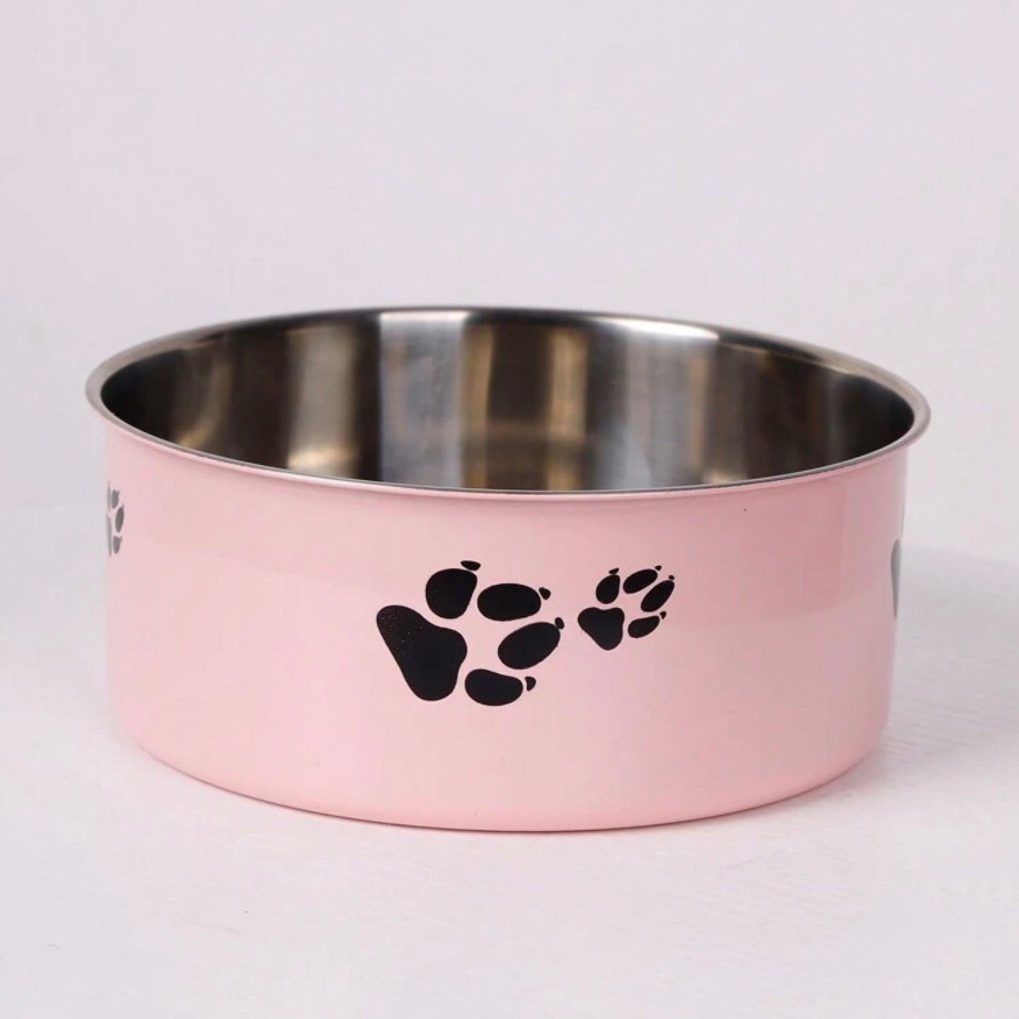 Pastel pink stainless steel pet bowl with black paw prints on the side, empty and placed on a white background.