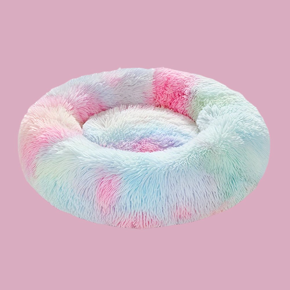 Empty fluffy pastel rainbow donut dog bed on a pink background.