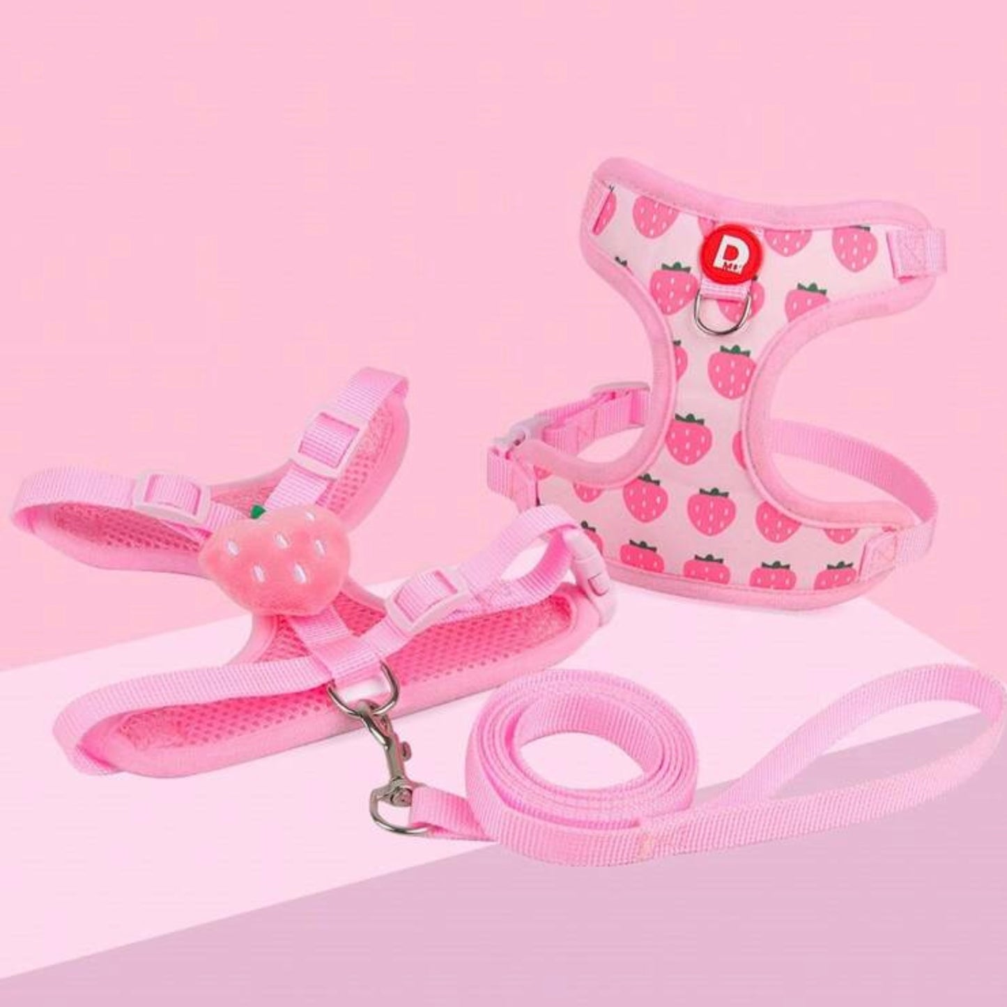 Pink pet harness and leash set with strawberry pattern, including a harness with a strawberry design, a matching leash, and a harness accessory shaped like a strawberry, displayed on a light pink background.