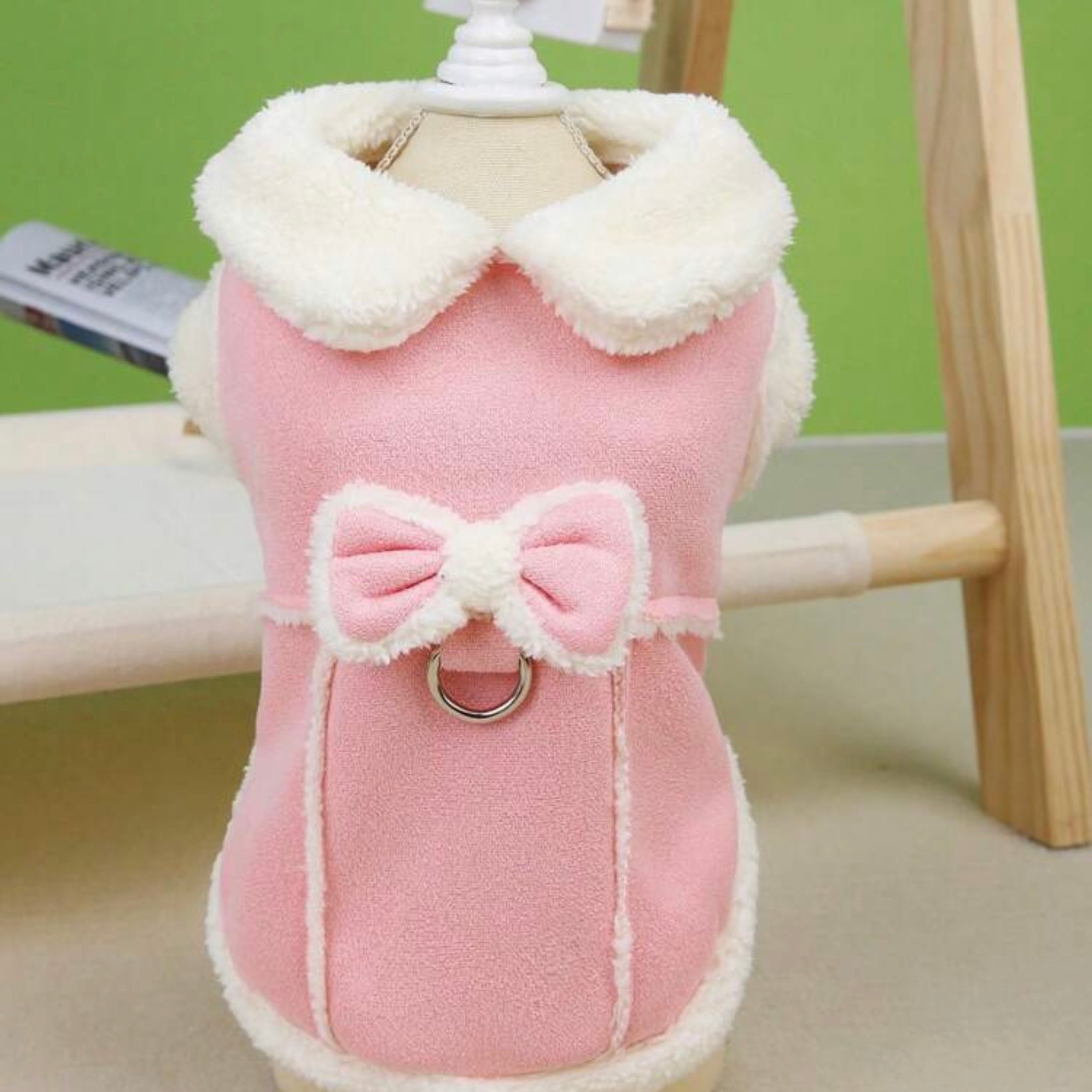 Pink dog jacket with white faux shearling collar and bow detail displayed on a mannequin.