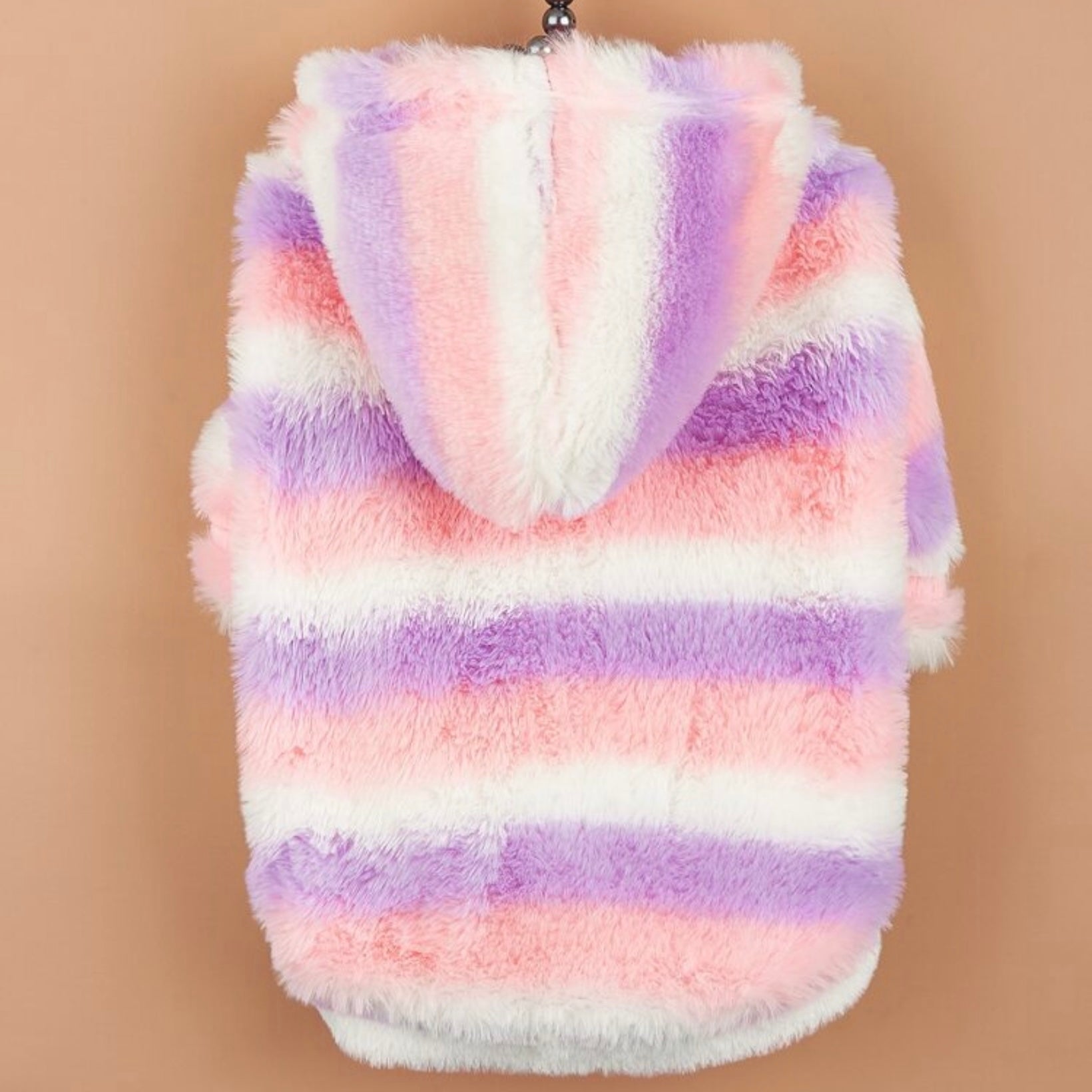 Back view of a pastel striped fluffy dog jacket with a hood, hanging on a hanger against a tan background.