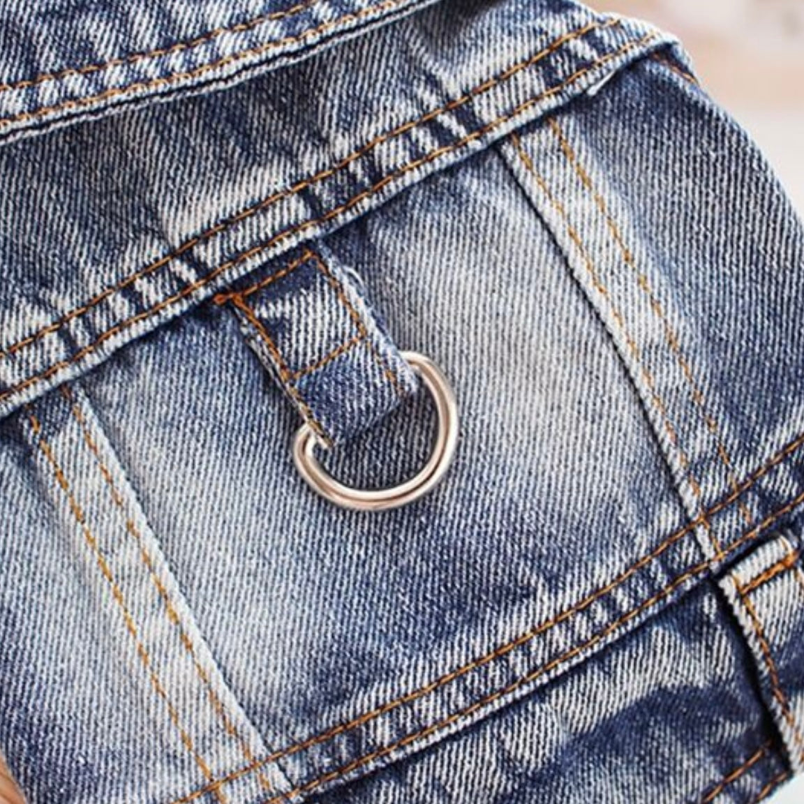 Close-up of the metal D-ring and stitching detail on the back of a blue denim dog jacket.