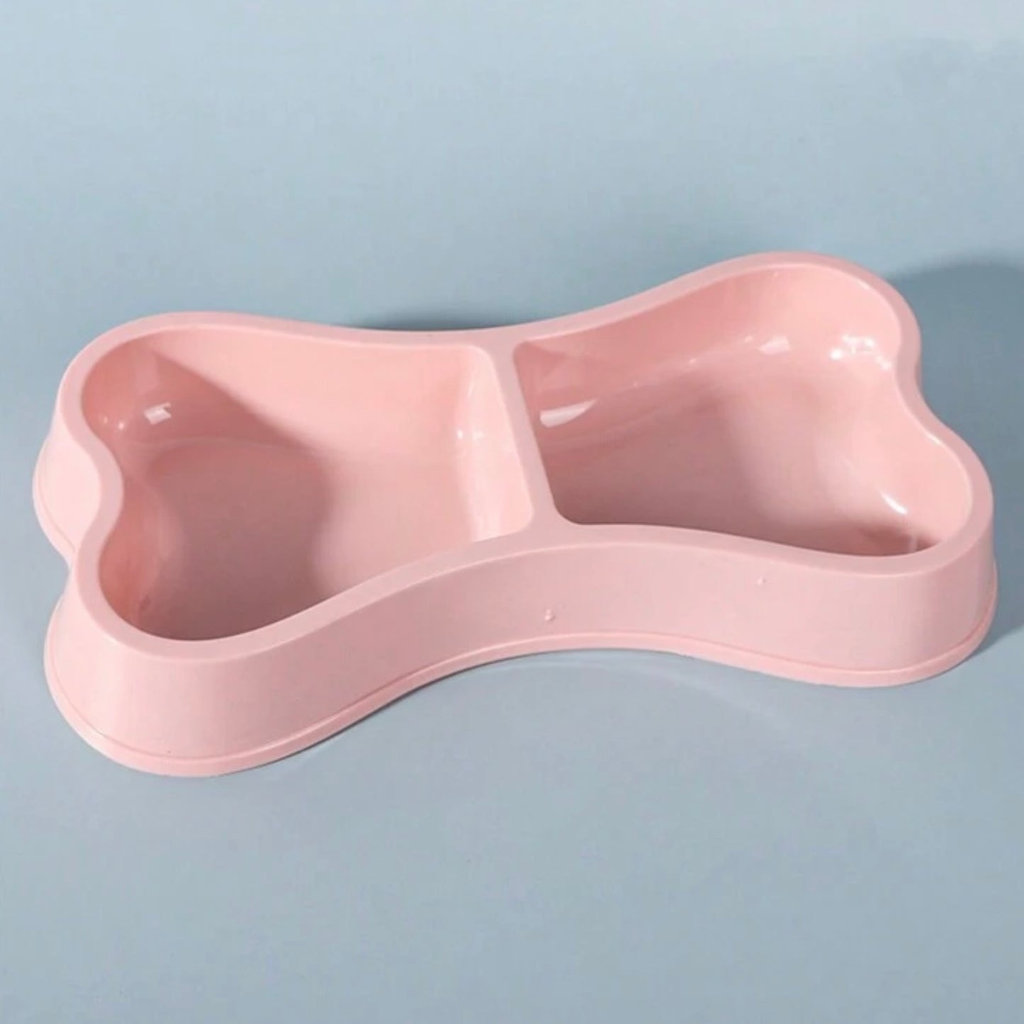 Close-up of a pink bone-shaped double dog bowl on a light blue background.