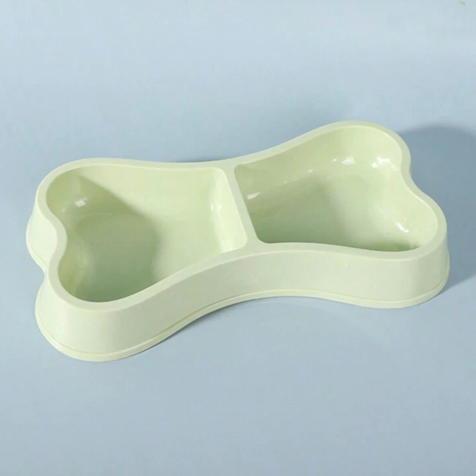 Close-up of a green bone-shaped double dog bowl on a light blue background.