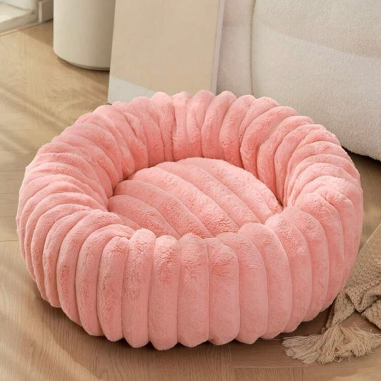 Plush ribbed donut dog bed in soft peach color on a wooden floor.