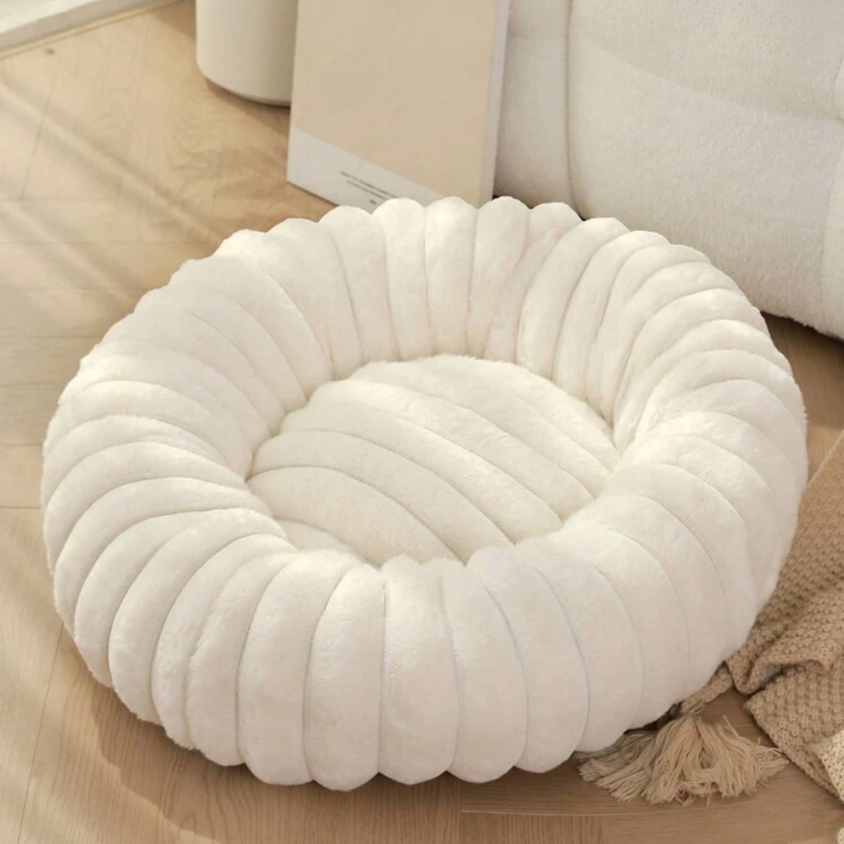 Plush ribbed donut dog bed in ivory white on a wooden floor.