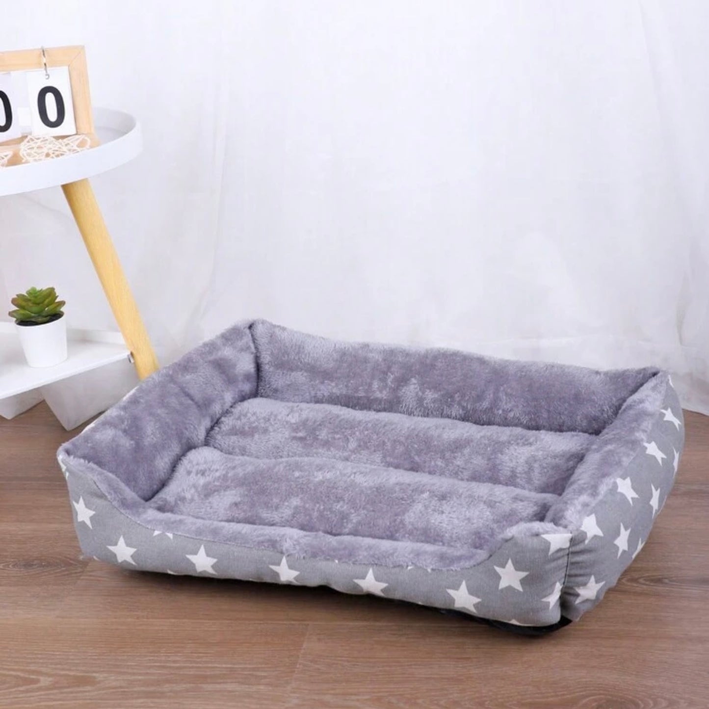 Empty grey star-patterned rectangular dog bed with plush interior on a wooden floor.