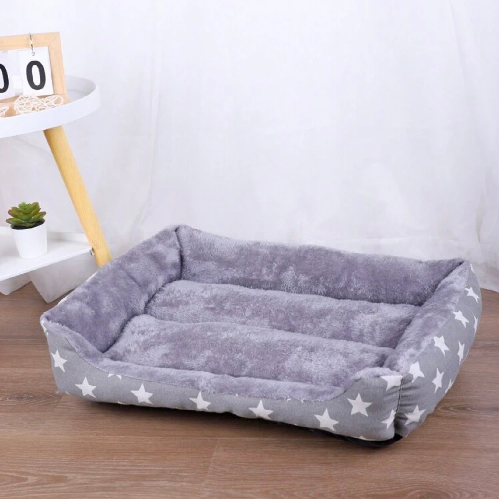Empty grey star-patterned rectangular dog bed with plush interior on a wooden floor.