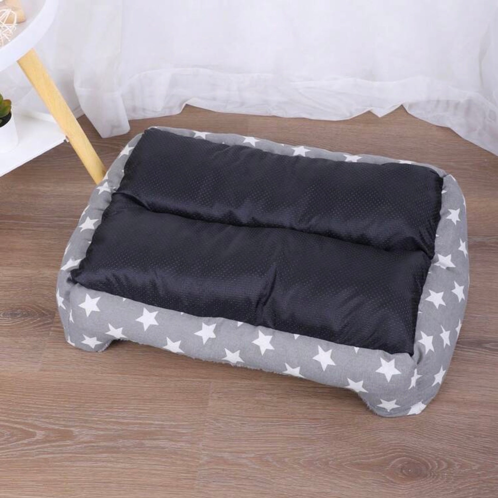 Grey star-patterned dog bed placed on a wooden floor.