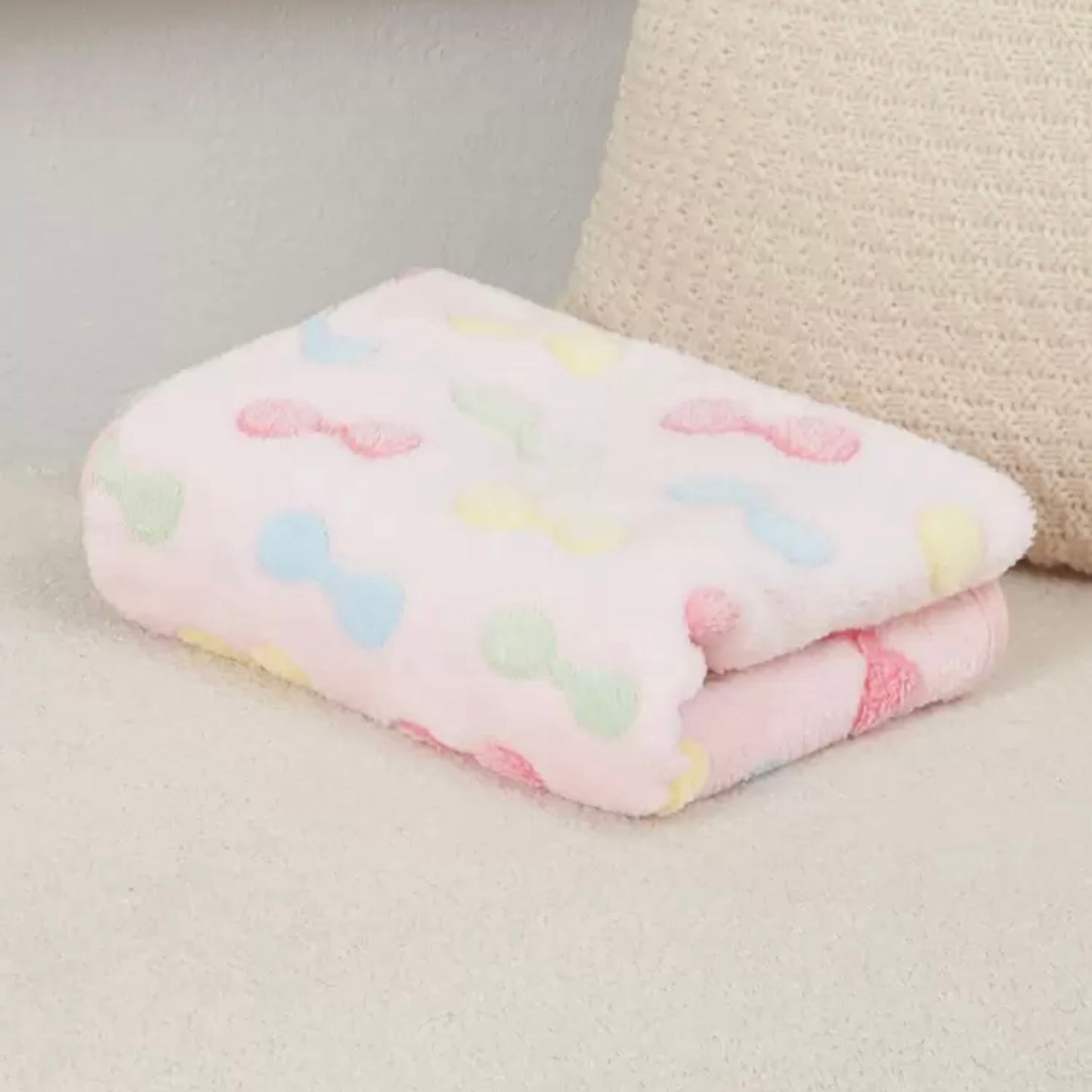 Soft dog blanket featuring pink, blue, yellow, and green bows, neatly folded.
