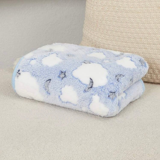Folded fluffy blue dog blanket with white clouds on a cream sofa.