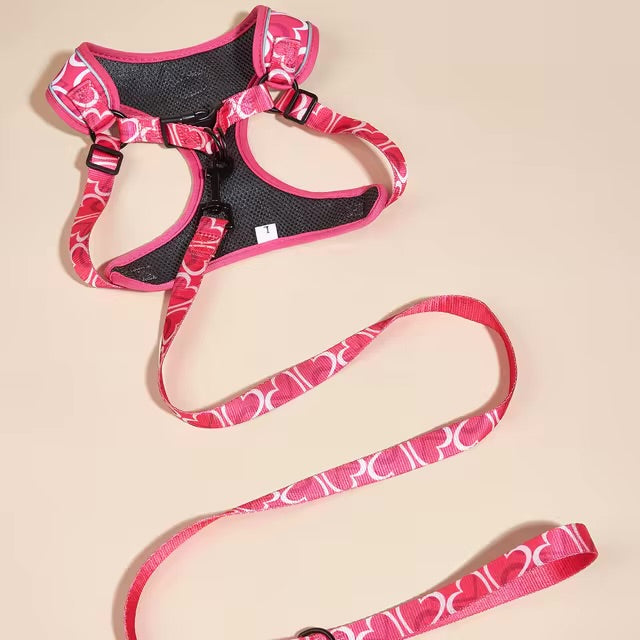 Pink dog harness and matching leash with a white heart pattern laid out on a light surface.
