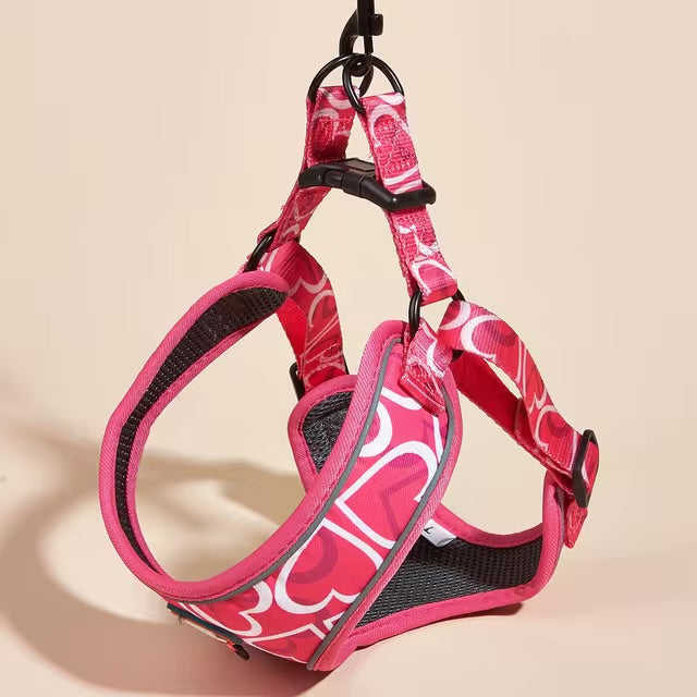 Pink dog harness with a white heart pattern hanging by its leash attachment ring.