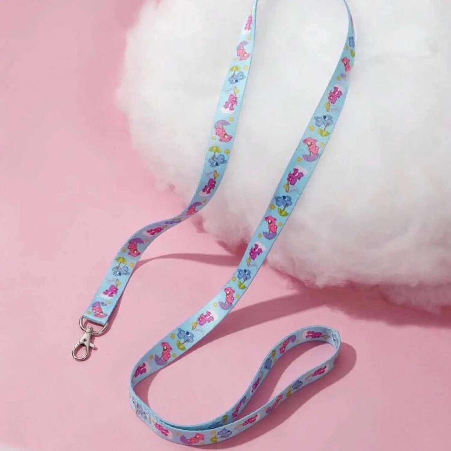 Blue dog leash with colorful Care Bears pattern, laid out on a pink background next to a fluffy white object.
