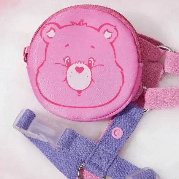 Pink Care Bears pouch attached to a purple and pink dog harness, displayed on a white background.