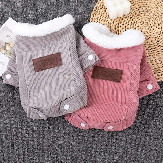 Two corduroy dog jackets, one grey and one pink, both with white fleece collars and brown patches, laid side by side on a textured grey surface.