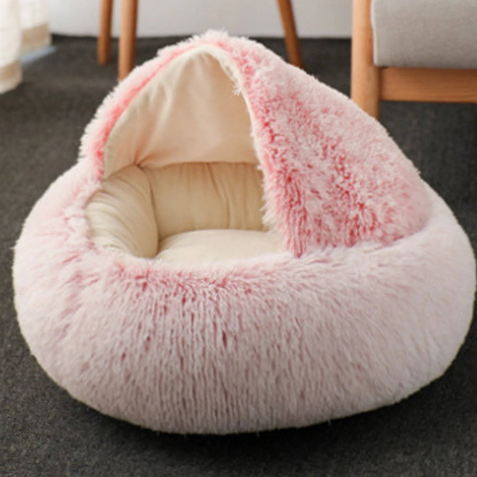 Light pink and cream plush dog cave bed with a semi-enclosed dome, placed on a dark carpet.