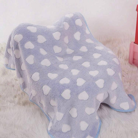Light blue dog blanket with white heart patterns draped over an object, on a soft furry surface.