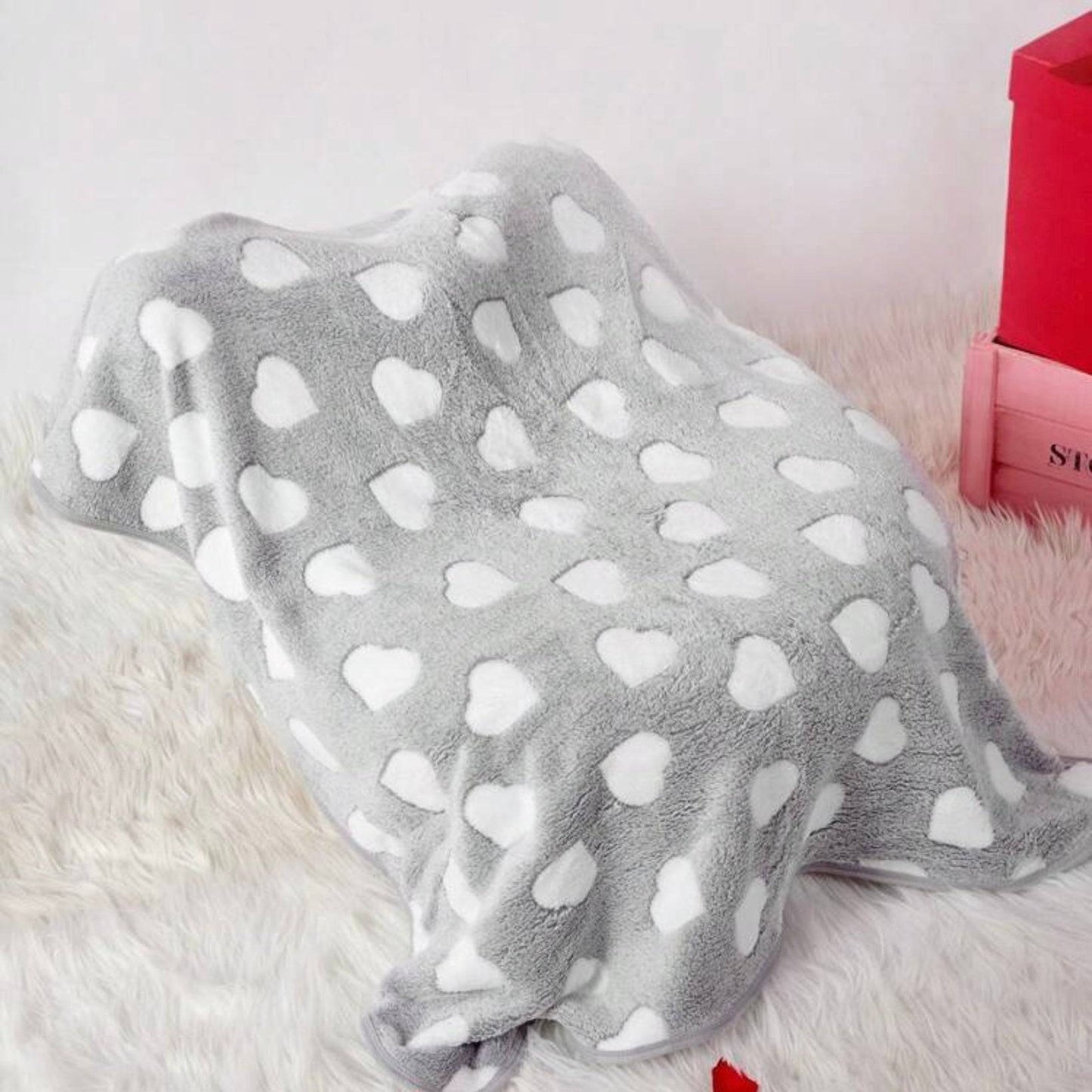 Gray dog blanket with white heart patterns draped over an object, on a soft furry surface.