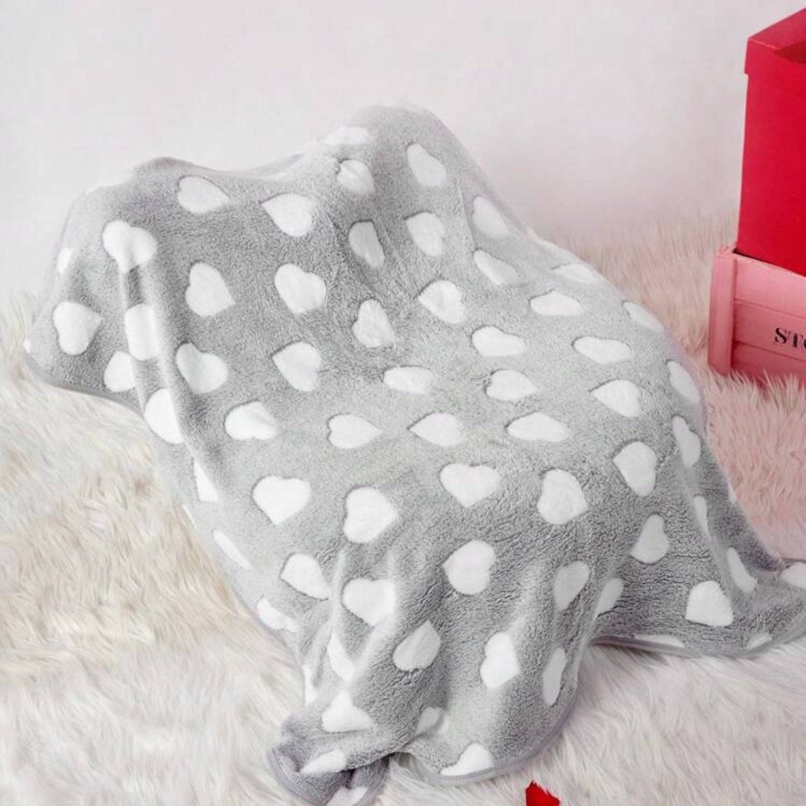 Gray dog blanket with white heart patterns draped over an object, on a soft furry surface.
