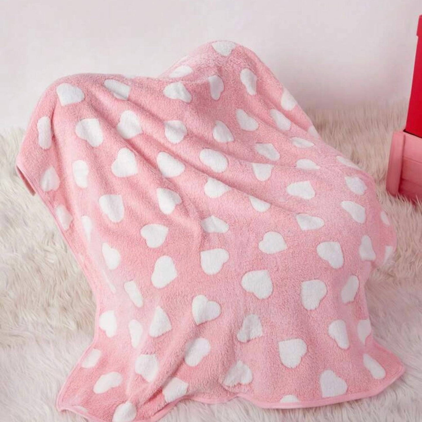 Pink dog blanket with white heart patterns draped over an object, on a soft furry surface.