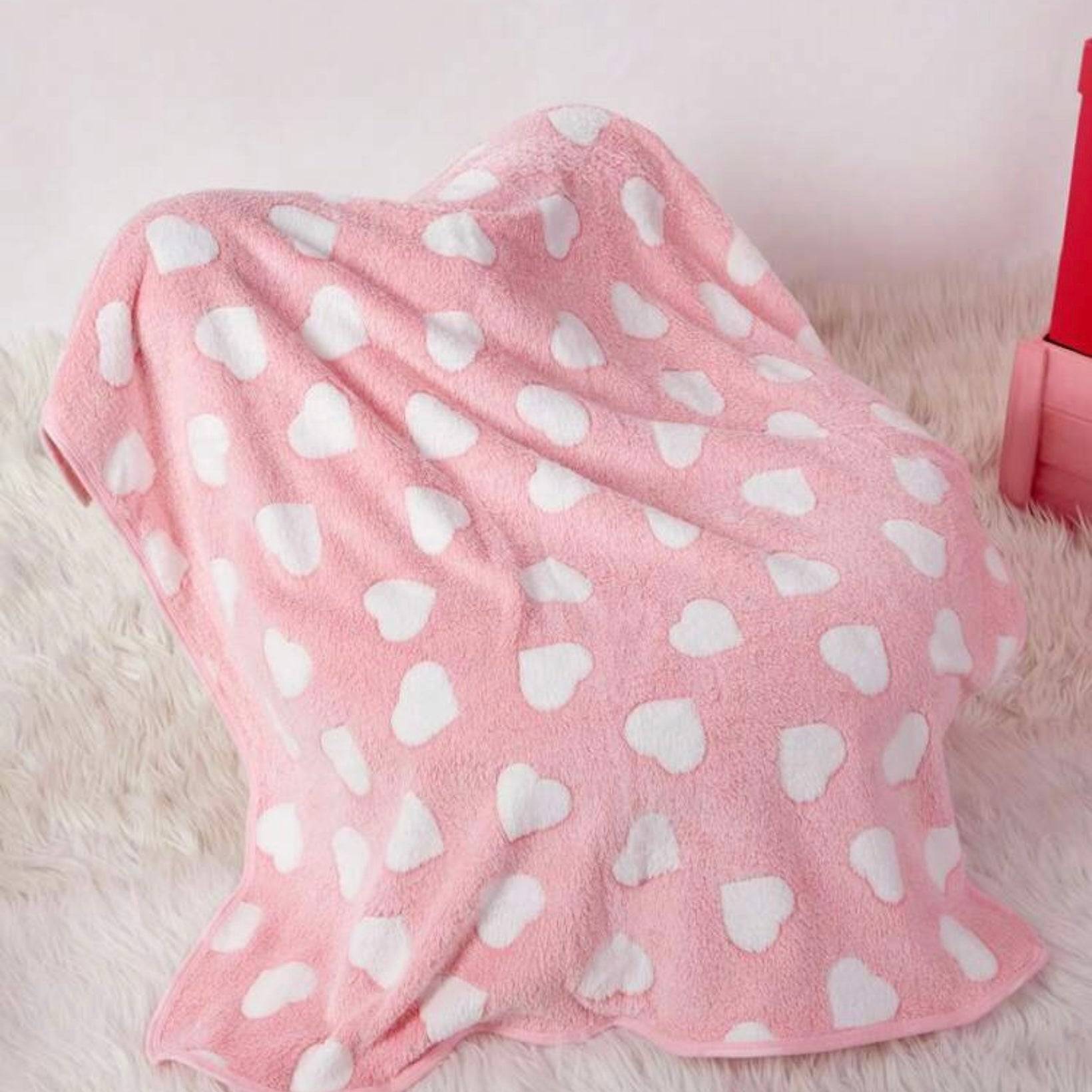 Pink dog blanket with white heart patterns draped over an object, on a soft furry surface.