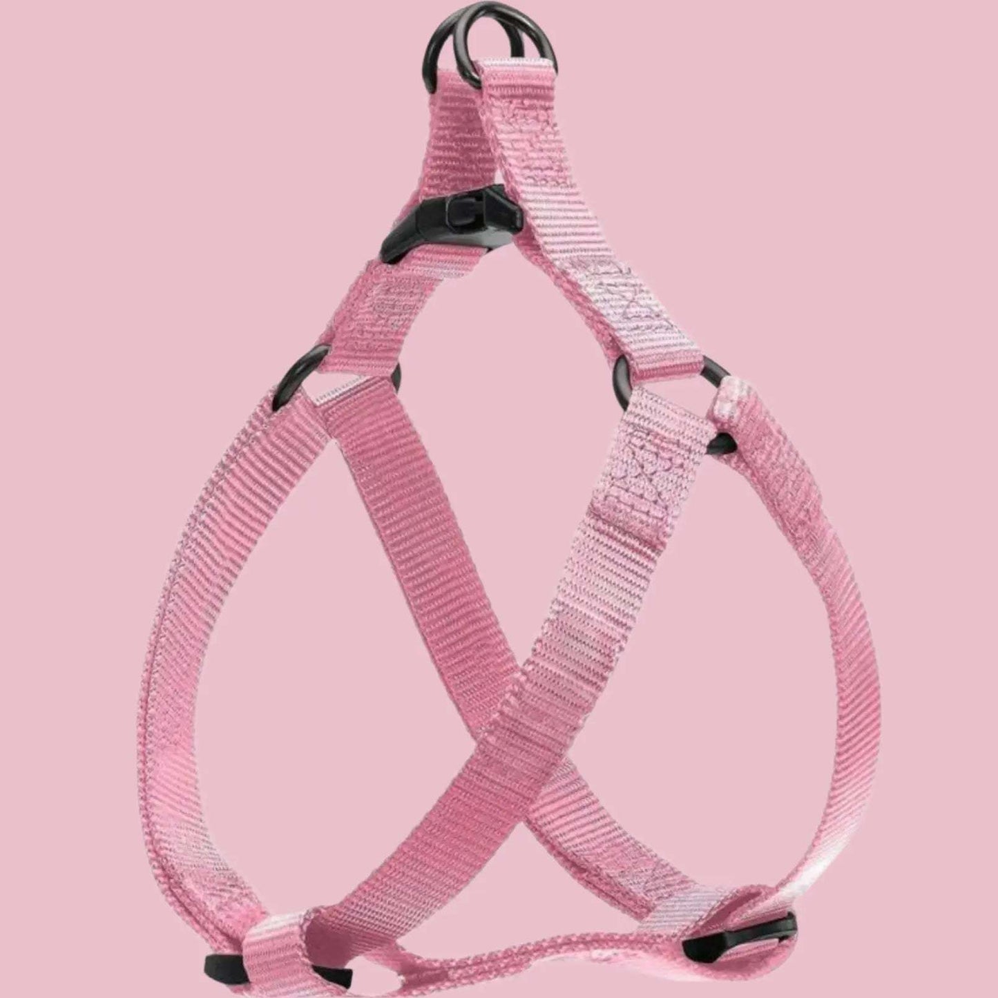 Pink adjustable step in dog harness with black plastic buckles and metal rings, displayed on a plain pink background.