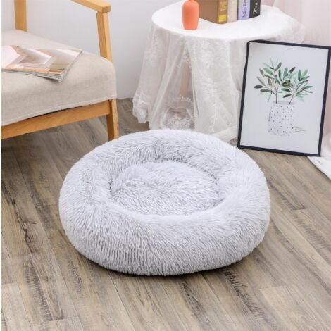 A round, fluffy, light gray dog bed on a wooden floor in a cozy living room setting.