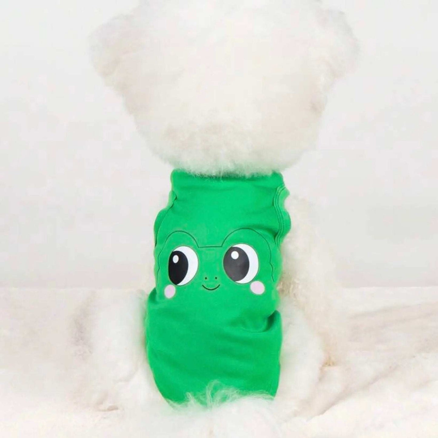 Back view of a fluffy white dog wearing a green shirt with a cartoon frog face design.