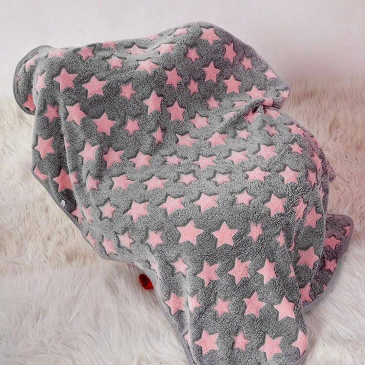 Grey dogblanket with pink stars draped over an object, on a soft cream rug.
